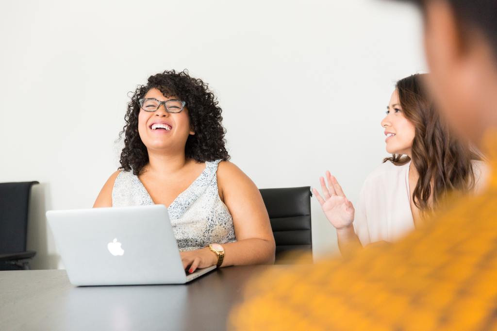 A woman laughs at a laptop.